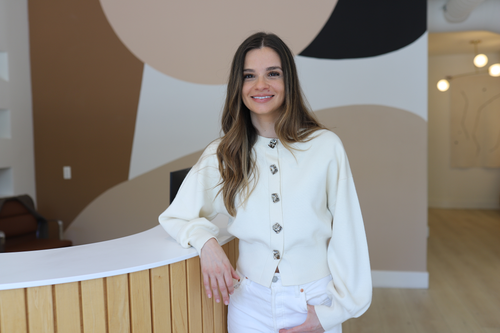 Dr. Vicky standing at the reception desk of a modern dental clinic with minimalist design and calm neutral colors.