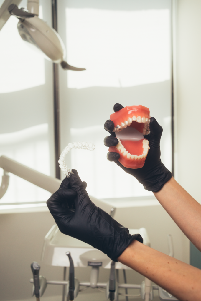 Close-up of a dental professional holding a clear aligner next to a detailed dental model, illustrating modern orthodontic treatment, teeth alignment solutions, and advanced cosmetic dentistry for a healthier, confident smile.