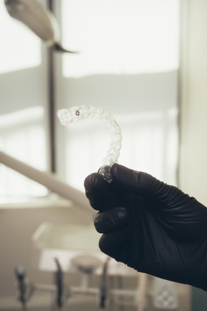 Hand in black glove holding clear dental aligner at SMILELOUNGE in Brooklyn, NY