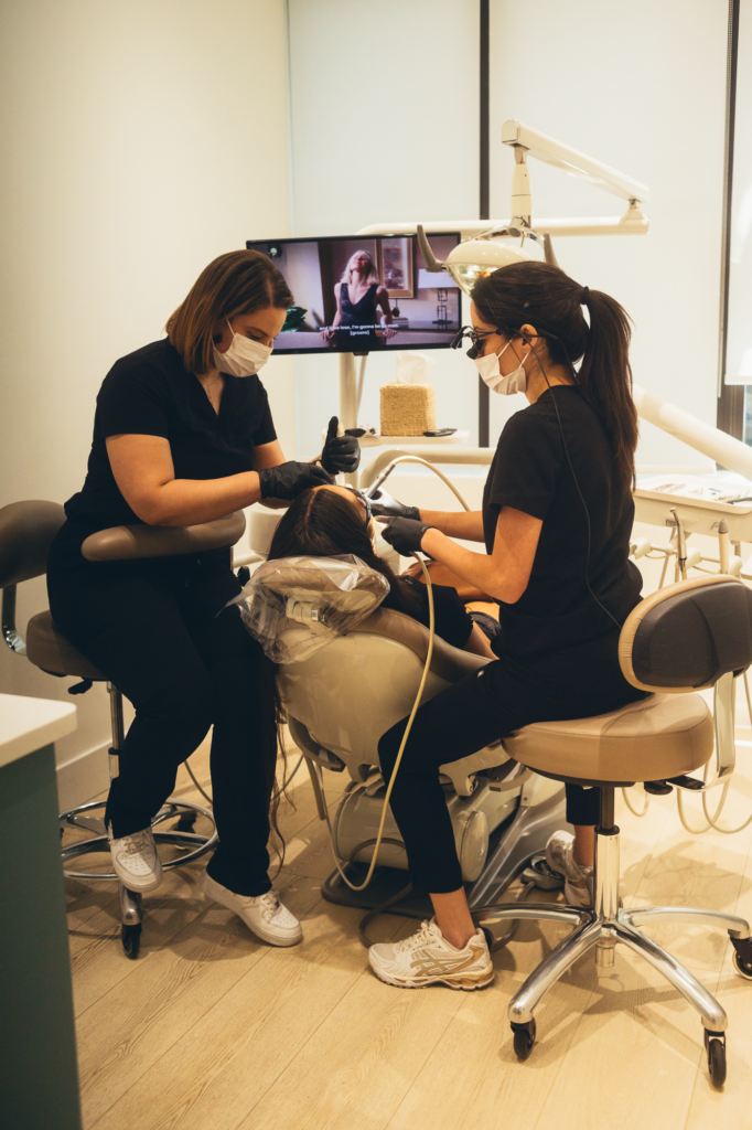 Two experienced dental professionals performing a comprehensive dental procedure on a patient in a modern, fully equipped dental clinic, highlighting advanced technology, professional oral care, and a comfortable patient-centered environment.