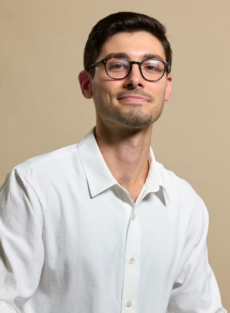 Smiling Dr. Grecco wearing glasses and white shirt at SMILELOUNGE in Brooklyn, NY
